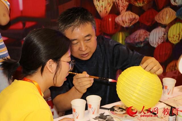 嘉年華現(xiàn)場青年向民間藝人學習如何畫彩燈