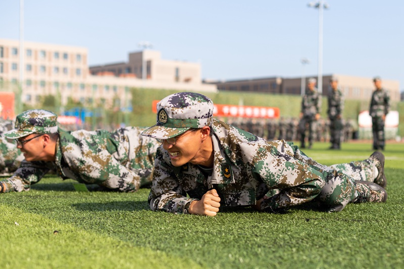 北京郵電大學(xué) 學(xué)生在滾燙的草地上匍匐前進(jìn)，咬牙完成15米訓(xùn)練（陳潤(rùn)濱/攝）