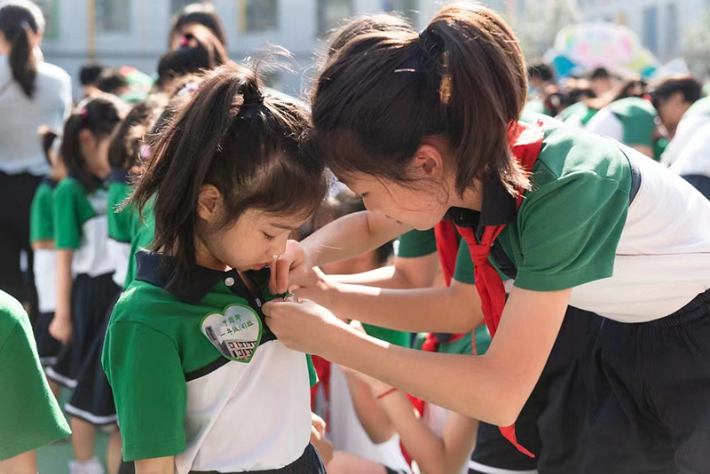 9月1日，芳草地國際學(xué)校以“走進(jìn)芳草-欣欣向榮”為主題舉辦開學(xué)典禮，圖為高年級(jí)學(xué)生為一年級(jí)同學(xué)佩戴學(xué)校校徽。北京市朝陽區(qū)教委供圖